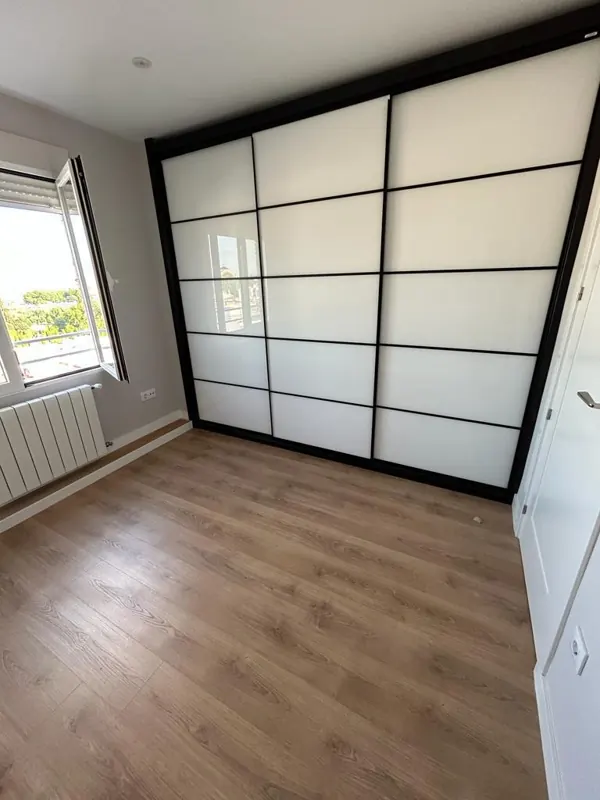 Puerta corredera tipo japonés de cristal translúcido separando salón y dormitorio, con suelo laminado